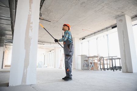 Construction worker applying a coat of paint on a wall using a roller, working diligently on a building siteの写真素材