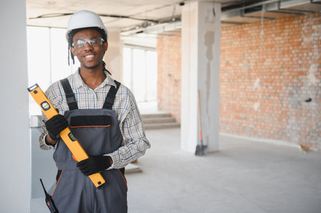 Young african american construction worker holding level tool smiling at camera inside building...