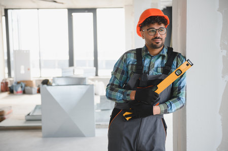 Arab engineer wearing protective workwear and holding a level tool inside a building under...