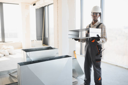 African american construction worker carrying ventilation pipes inside a building under construction