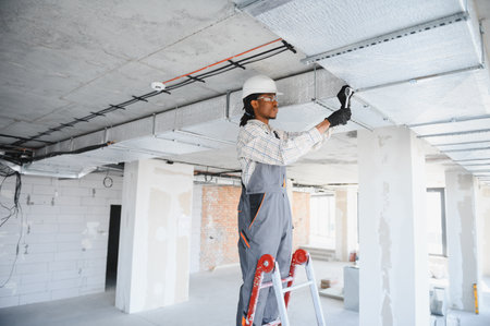 African american construction worker installing ventilation pipes at a construction site, focusing on hvac systems for efficient airflow and comfortの写真素材