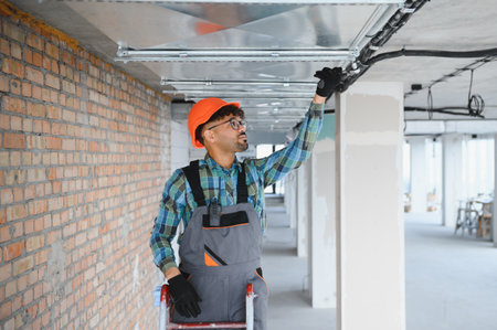 Arab engineer wearing safety helmet and overall inspecting ventilation system on construction site