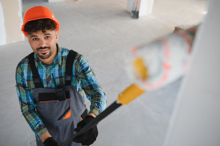 Arab construction worker painting a wall using a long roller brush, working on a renovation project