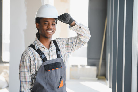 African american construction worker smiles while adjusting his hardhat at a brightly lit construction siteの写真素材
