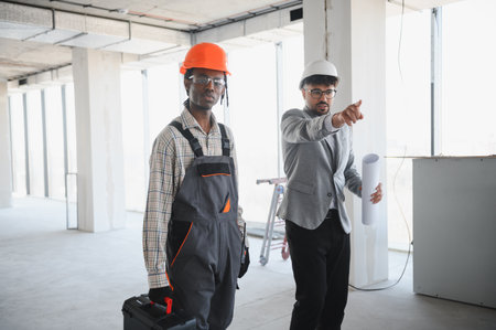 Architect holding blueprints showing instructions to builder carrying toolbox during building...