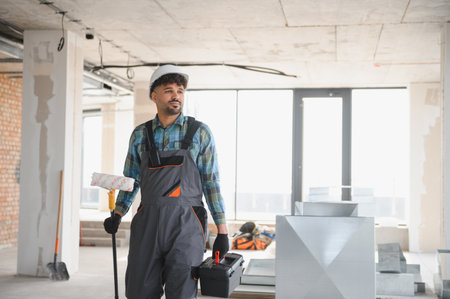 Arab engineer walking inside a building under construction carrying a paint roller and a toolbox