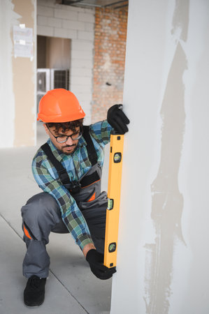 Arab construction worker checking vertical alignment of a wall using a spirit level, ensuring...