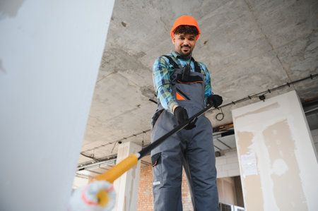 Smiling arab builder painting walls and ceiling using a telescopic paint roller during house...