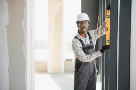 Smiling african american construction worker using spirit level while installing window frame at...