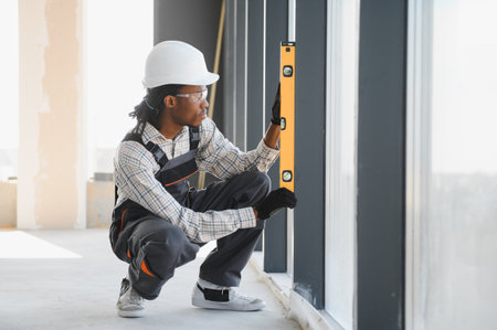Young african american construction worker checking window level with spirit level inside a building...
