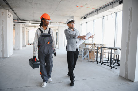 Architect walking through a construction site, discussing blueprints with a builder while inspecting...