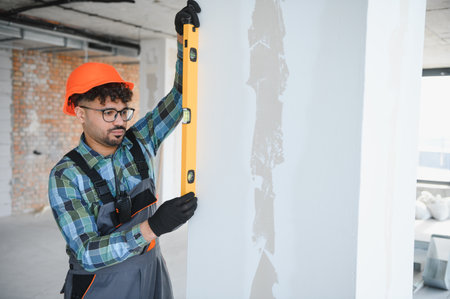 Focused engineer meticulously checks wall verticality with a spirit level, demonstrating precision...