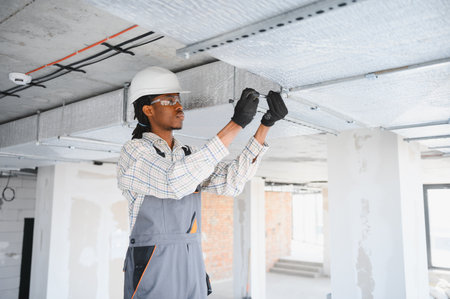 African american construction worker installing ventilation pipes on a construction site, using a...