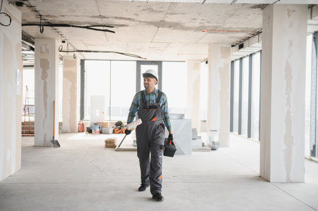 Arab engineer walking inside a building under construction carrying work tools and wearing safety...