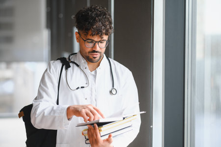 Focused medical student reviewing textbooks in university hallway, preparing for exams and medical...