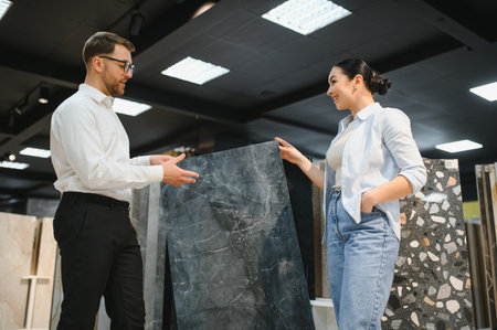 Salesman displaying a ceramic tile while discussing options with a female customer in a building materials store, highlighting quality and styleの写真素材