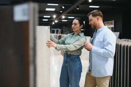 Couple carefully selecting ceramic tiles in a hardware store, planning their home renovation projectの写真素材