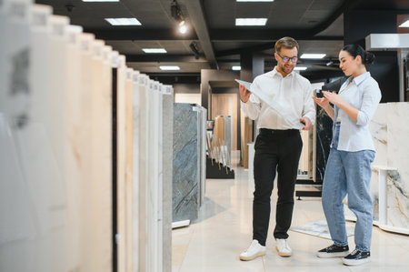 Salesman showing ceramic tile to customer in tiling and plumbing store, discussing and choosing materials for renovationの写真素材
