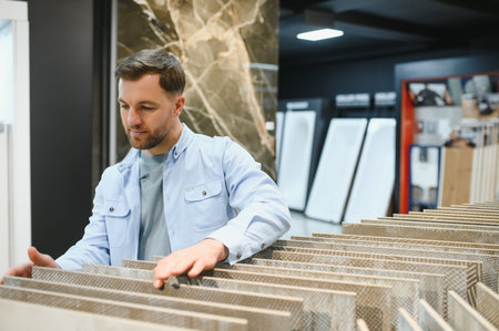 Man selecting ceramic tiles in a home improvement store, touching samples and making a decision for his renovation projectの写真素材
