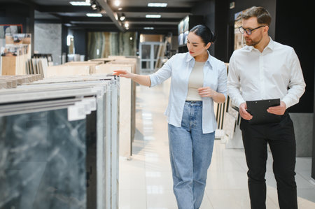 Female buyer discusses ceramic tile options with a male seller in a modern plumbing store, showcasing a variety of materials and designsの写真素材