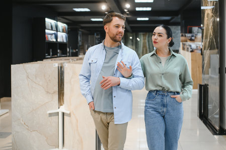 Couple walking and choosing ceramic tiles in a hardware store, discussing their home renovation projectの写真素材