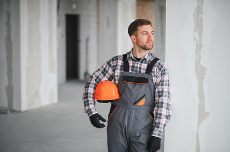 Construction worker wearing an orange helmet and smiling at the camera inside a building under...