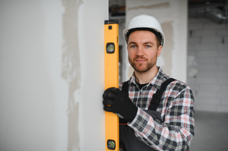 Builder wearing protective helmet and gloves uses a spirit level during renovation or construction...