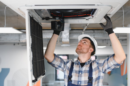 Hvac technician wearing hardhat and using screwdriver while repairing air conditioning unit on...
