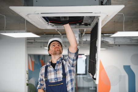 Hvac technician wearing a safety helmet and gloves is repairing an air conditioning unit on the...
