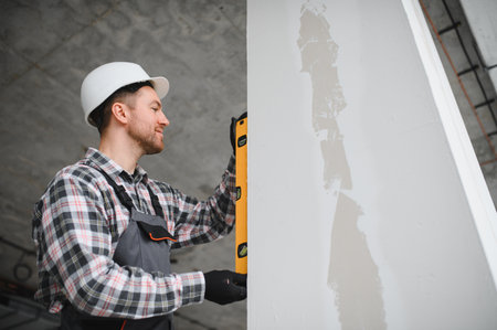 Builder using spirit level ensuring precise vertical alignment during building construction or...