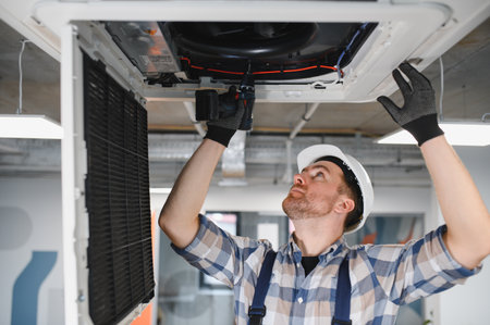 Hvac technician wearing safety helmet and work overalls installing an air conditioning unit using a cordless drillの写真素材