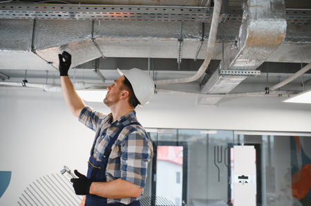 Hvac technician inspecting metal air ducts during installation of ventilation system in a building under constructionの写真素材