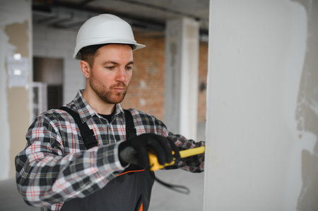 Builder wearing protective helmet and gloves using tape measure during renovation or construction workの写真素材