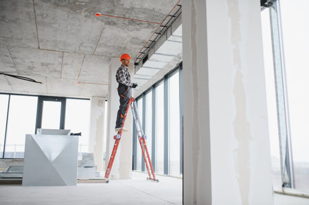 Builder with helmet working on ventilation system using a ladder in a building under constructionの写真素材