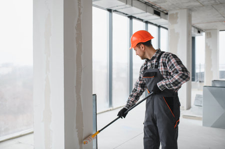 Professional builder using a paint roller, applying a fresh coat of paint to the walls of a building...