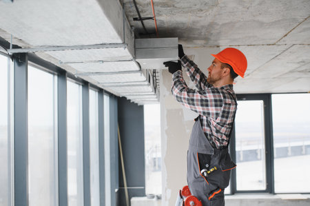 Builder with orange helmet installing an air conditioning system in a building under construction