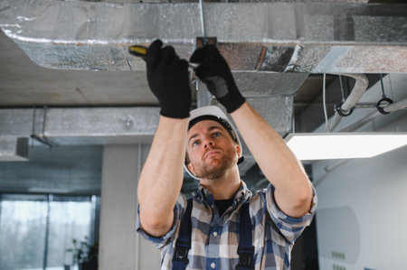 Hvac technician tightening screws while installing or repairing ventilation system ductwork,...