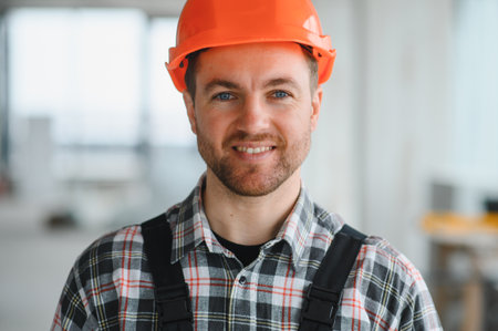 Construction worker wearing an orange helmet and smiling at the camera inside a building under...