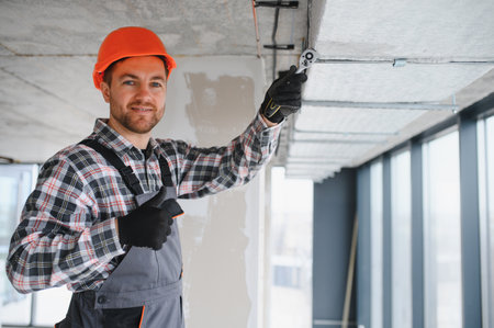 Builder wearing overalls and hardhat is using a ratchet wrench to tighten ventilation pipes in a...