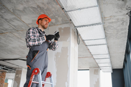 Construction worker installing hvac system on a ladder, working on ventilation in building under...