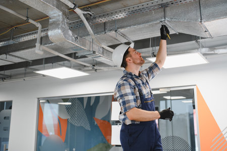 Builder wearing safety helmet and overall, checking ventilation pipes during repair works in a...
