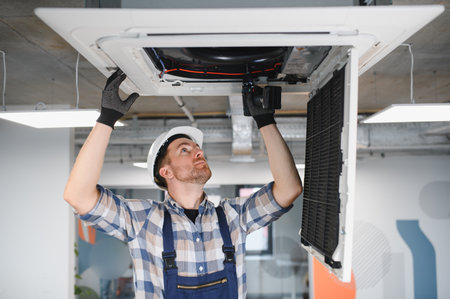 Hvac technician inspecting and repairing a ceiling mounted air conditioning unit, ensuring proper...