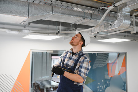 Hvac technician wearing safety helmet and gloves, inspecting air conditioning system during...