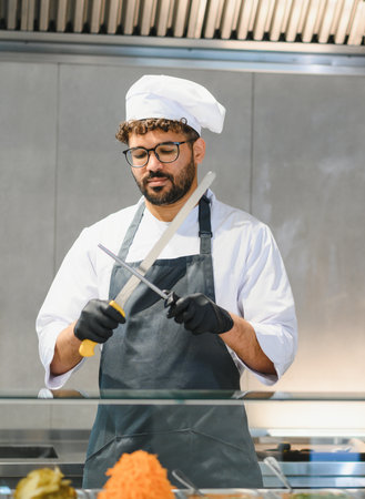 Professional chef sharpening knife, preparing to make kebabs or shawarma in a commercial kitchen