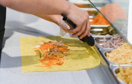 Cook adding pickled cucumbers and carrots to a lavash wrap with tongs, preparing a shawarma or kebab...