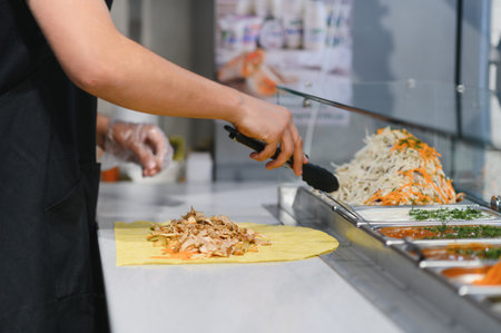Cook adding chicken and vegetables to a shawarma or kebab using tongs in a fast food restaurant...