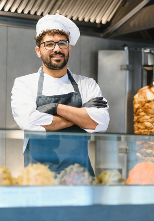 Confident chef wearing black gloves and apron crossing arms, smiling in his food truck, with...