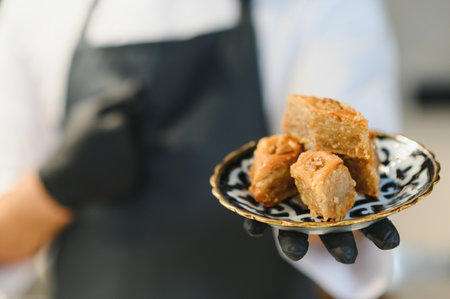 Chef wearing black gloves presenting baklava portions on an elegant plate, highlighting expertise in...