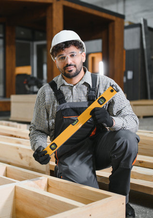 Middle eastern carpenter using spirit level while working on prefabricated house structure in...