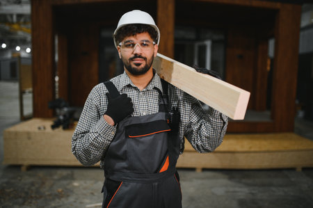 Arab construction worker carrying wooden plank on shoulder, working on prefabricated house in modern...